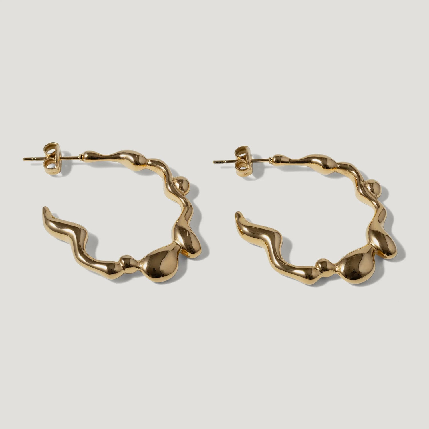 Pair of wavy gold hoop earrings with organic, sculptural design on white background
