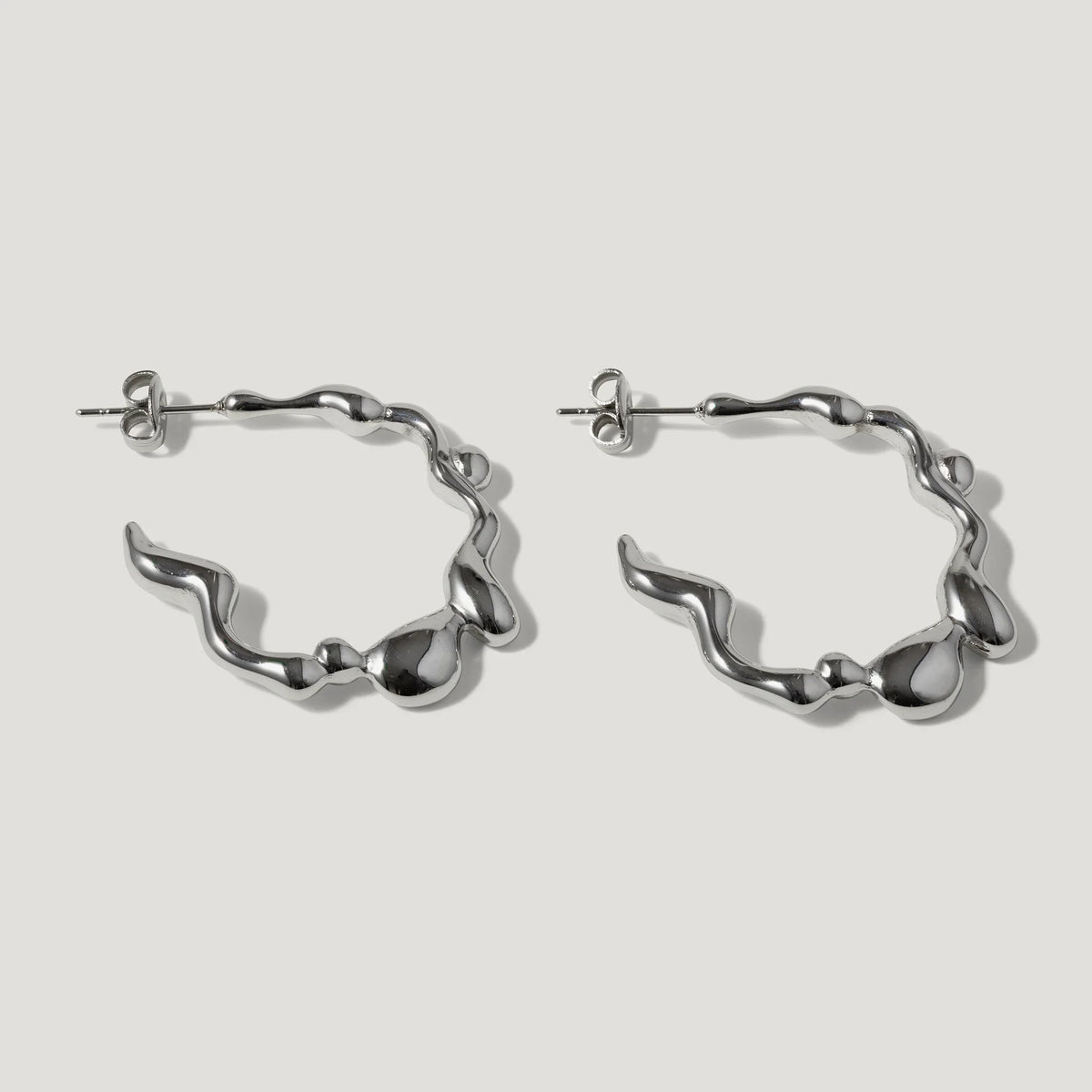 Pair of silver wavy hoop earrings with organic, fluid shapes on a white background
