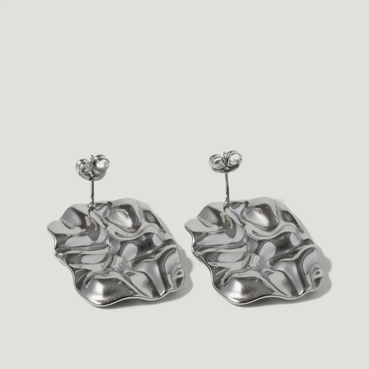 Silver sculptural earrings with organic, wavy shapes on a plain background