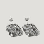 Silver sculptural earrings with organic, wavy shapes on a plain background