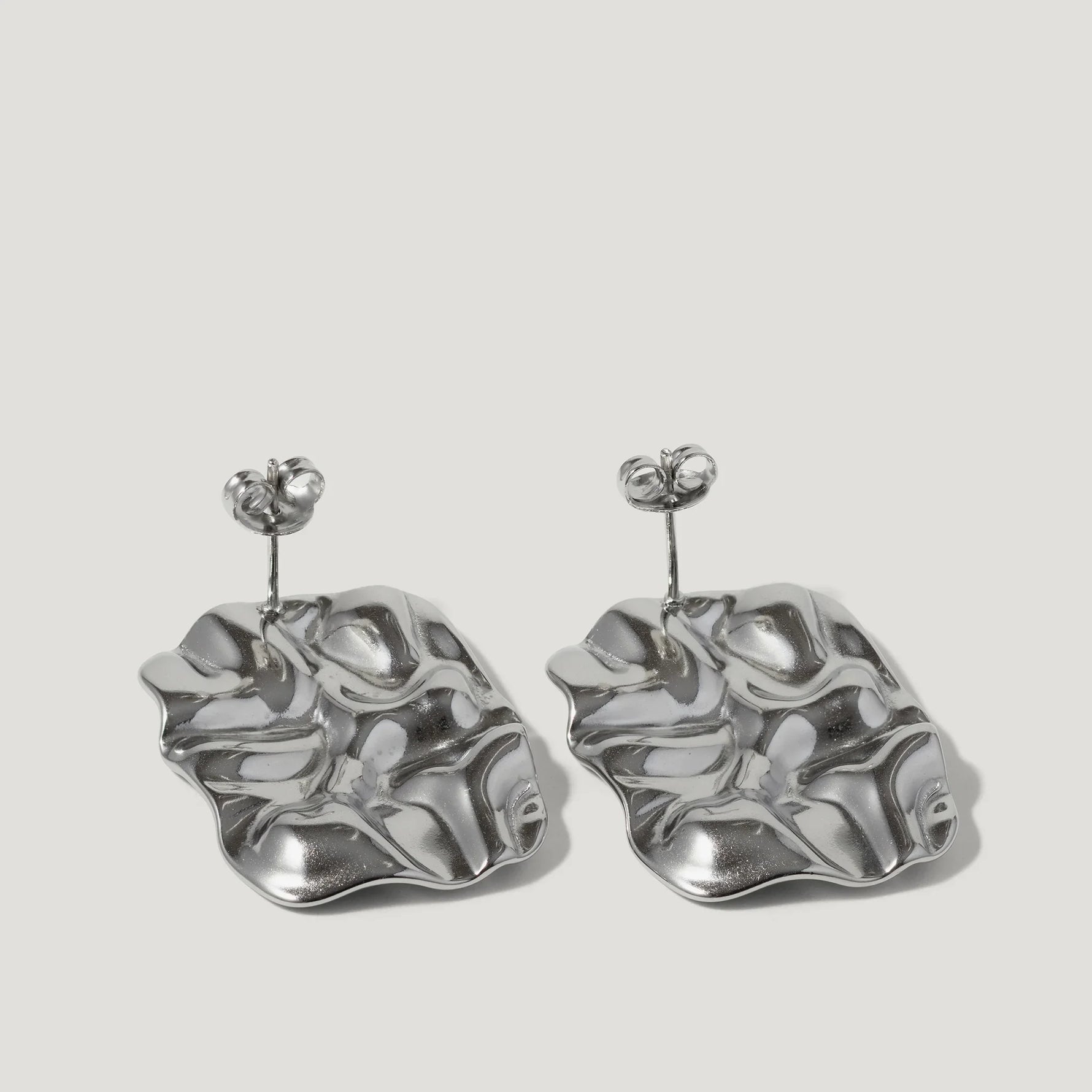Silver sculptural earrings with organic, wavy shapes on a plain background