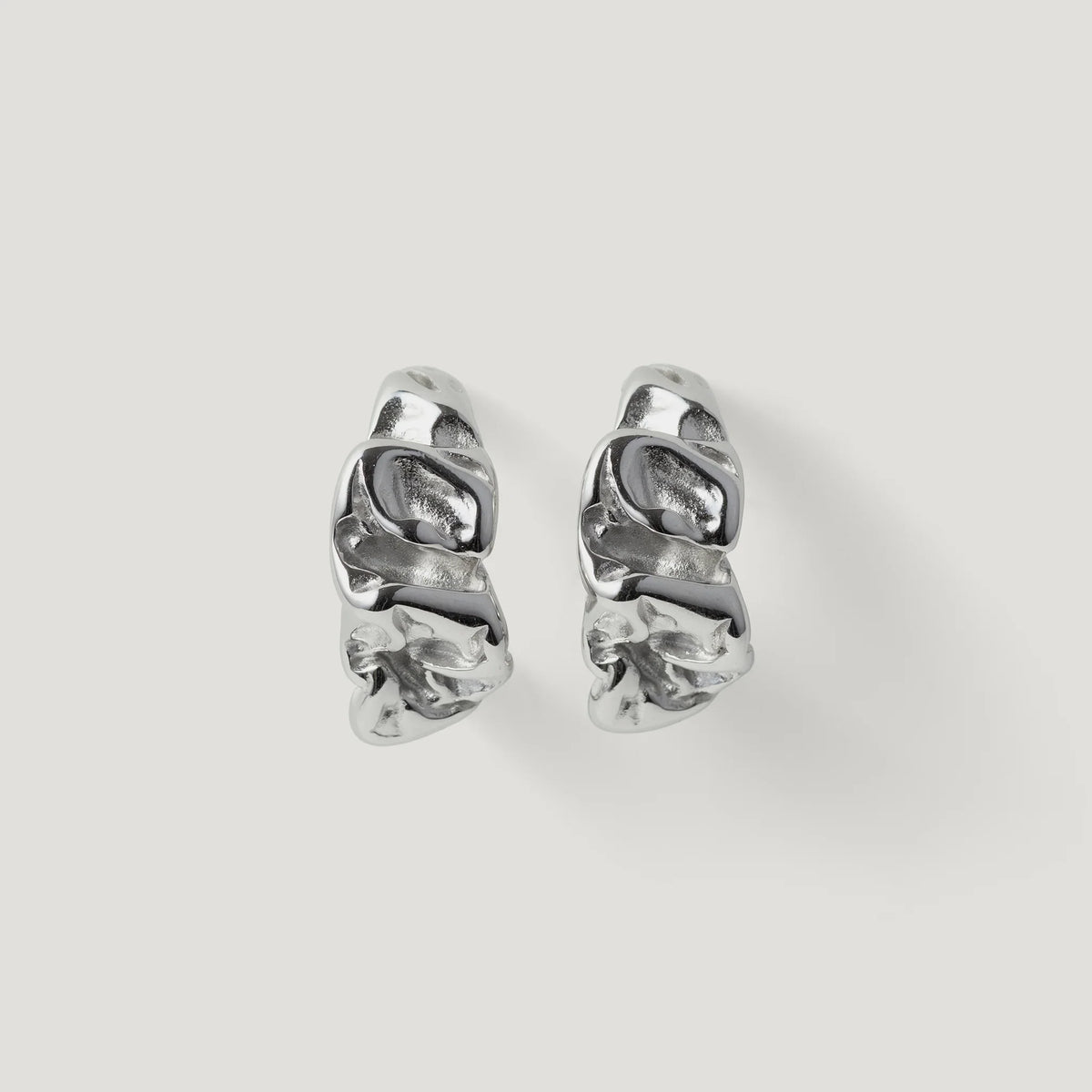 Pair of silver textured hoop earrings with organic, sculptural design on white background