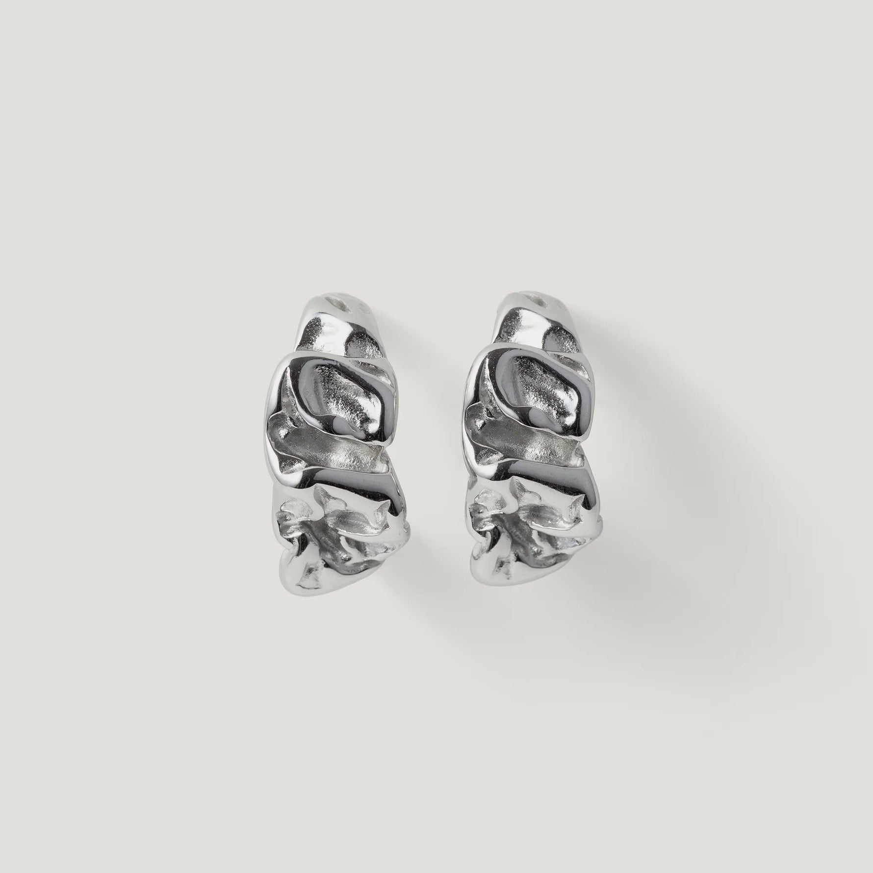 Pair of silver textured hoop earrings with organic, sculptural design on white background