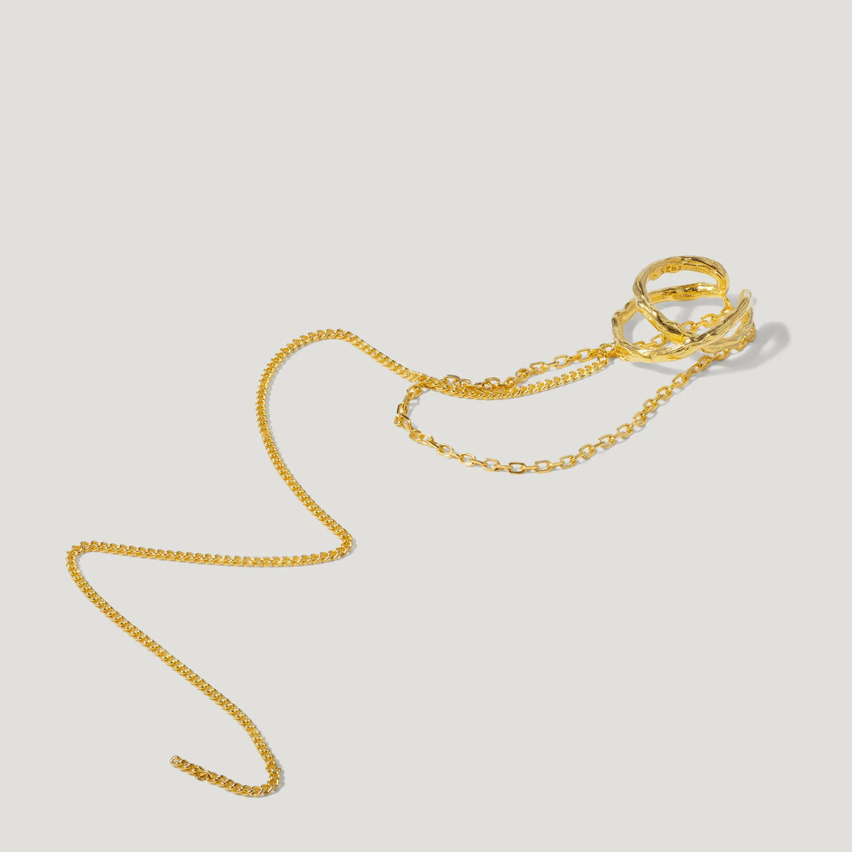 Gold ring with layered bands attached to delicate gold chain on white background