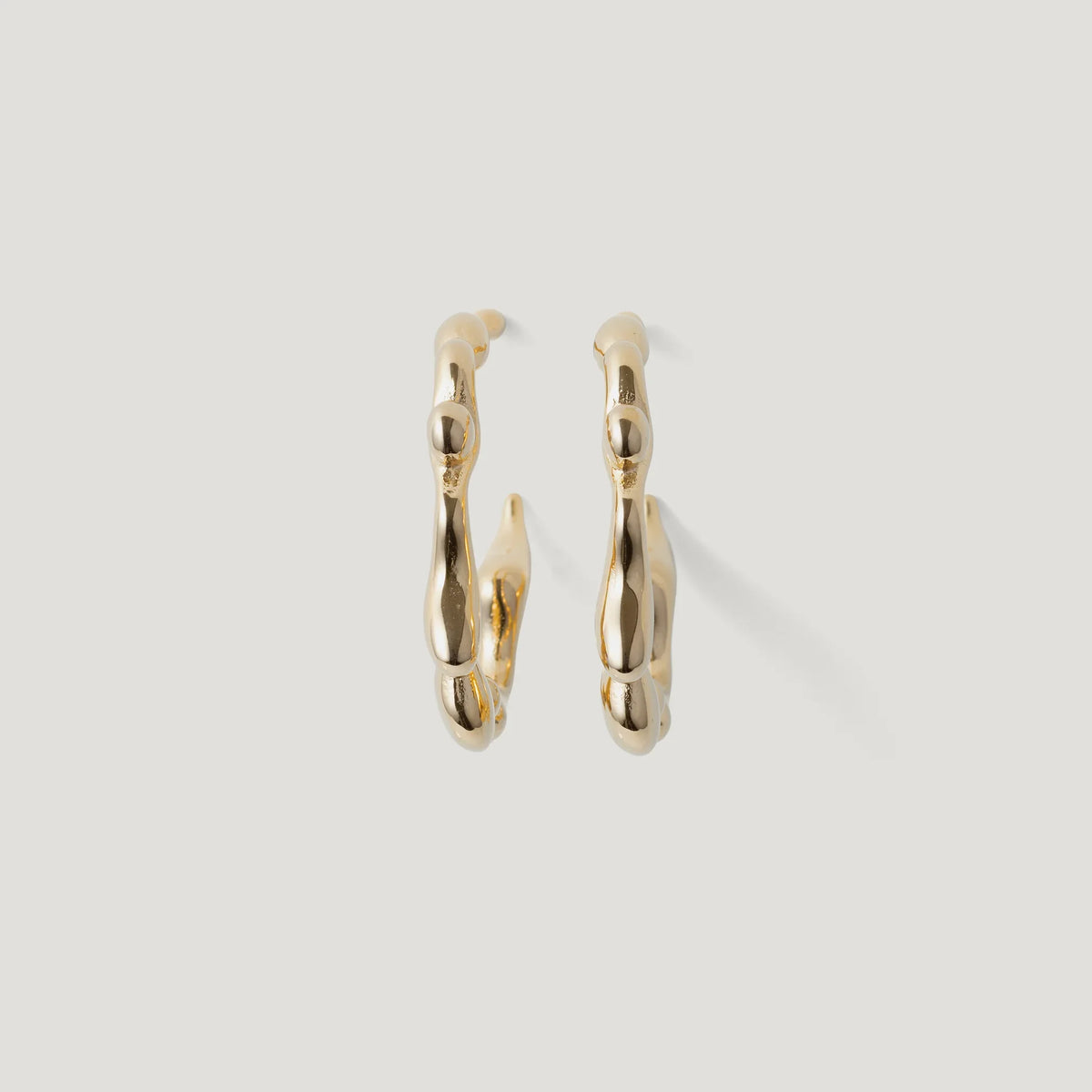 Pair of gold hoop earrings with organic, textured design on white background