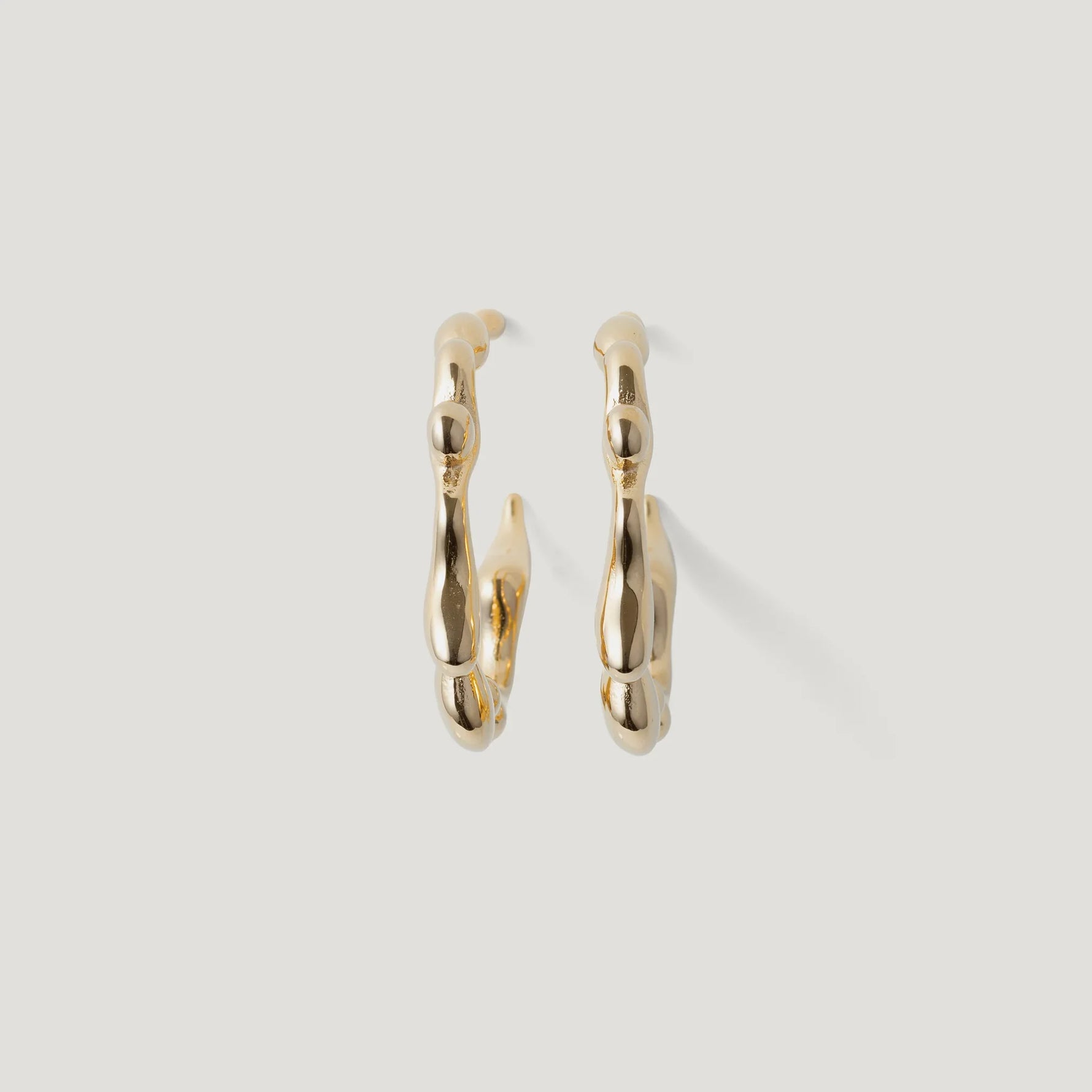Pair of gold hoop earrings with organic, textured design on white background