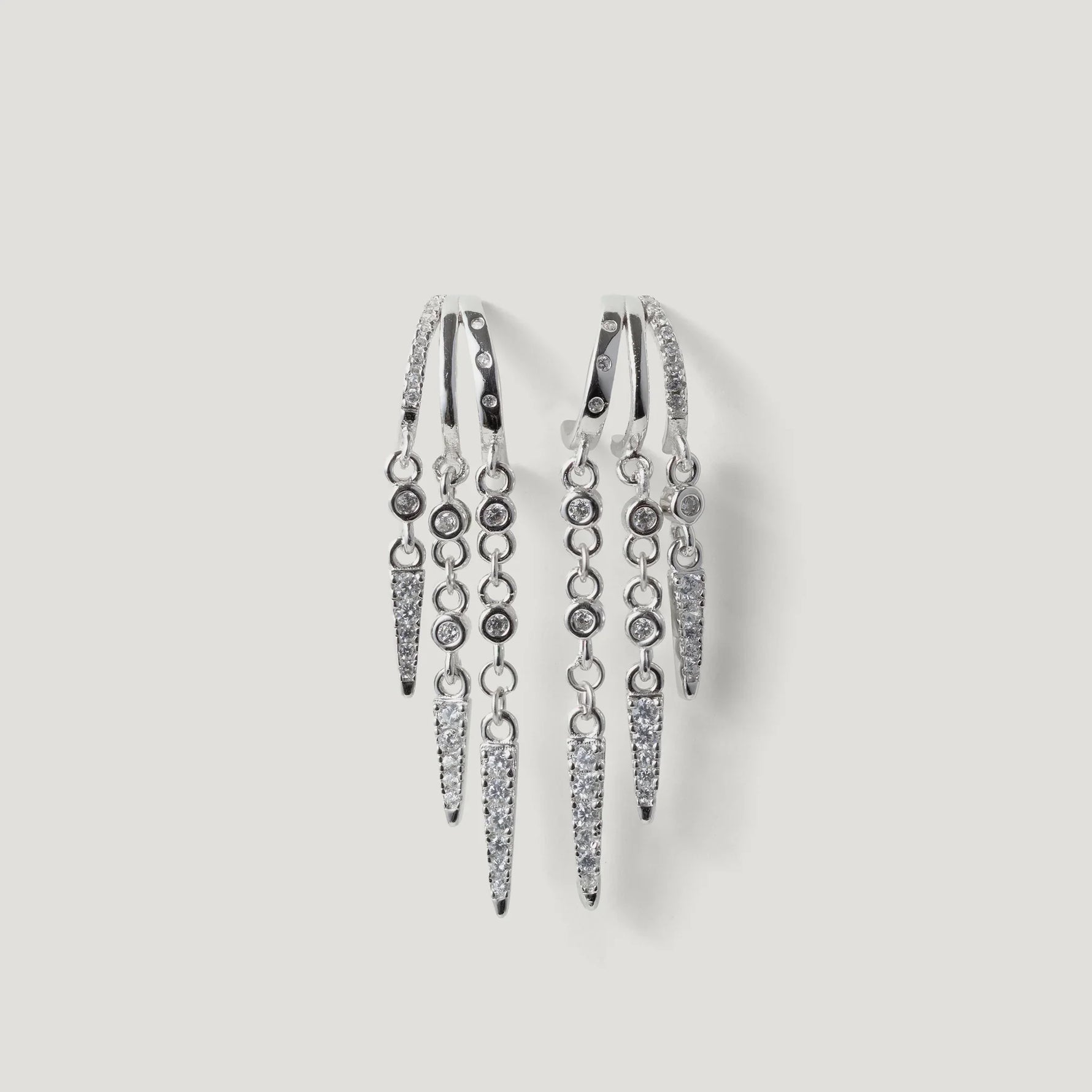 Silver hoop earrings with multiple dangling spike and round crystal accents on white background