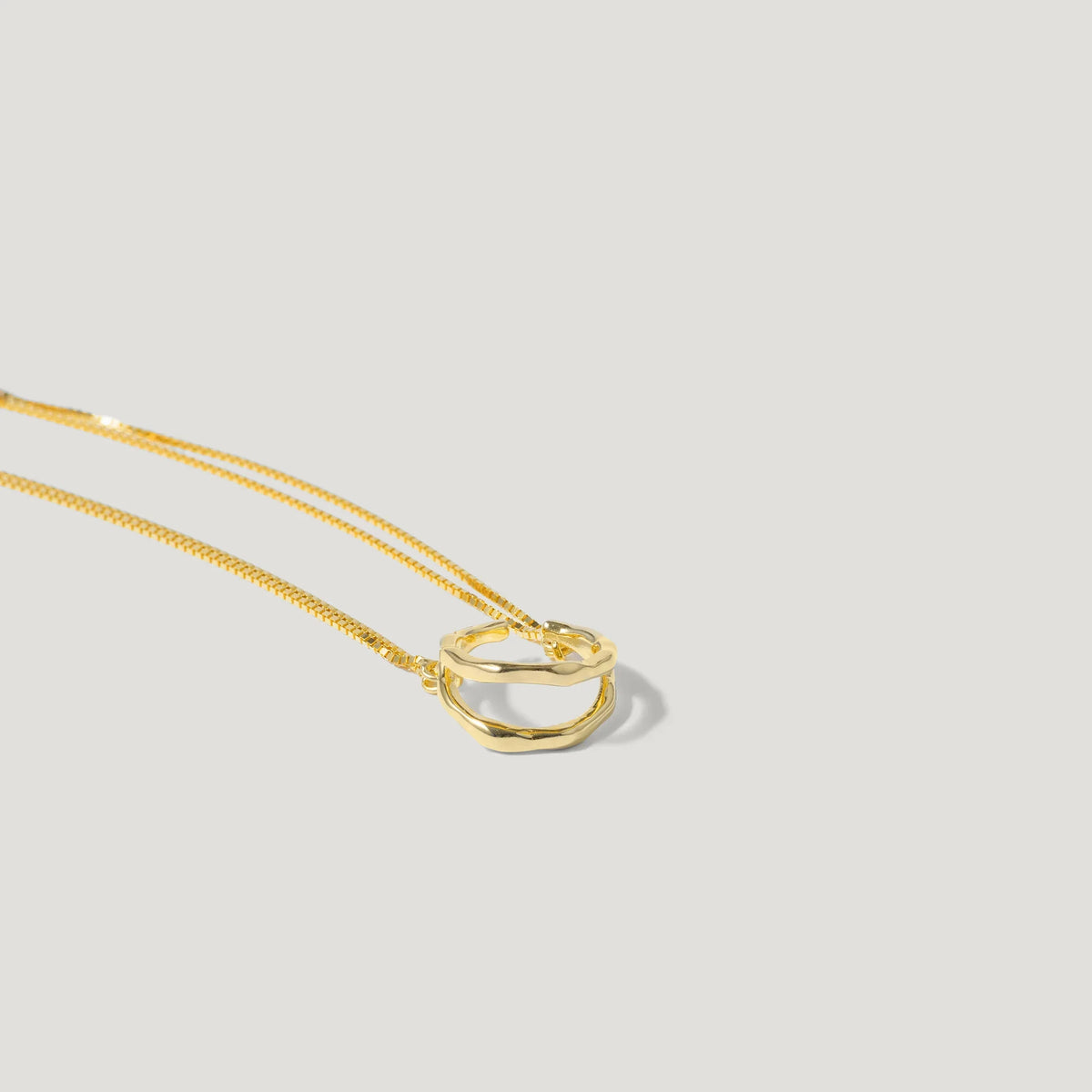 Gold chain necklace with two interlinked wavy gold rings on a light background