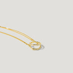 Gold chain necklace with two interlinked wavy gold rings on a light background