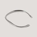 Minimalist silver cuff bracelet with a smooth, wavy design on a white background