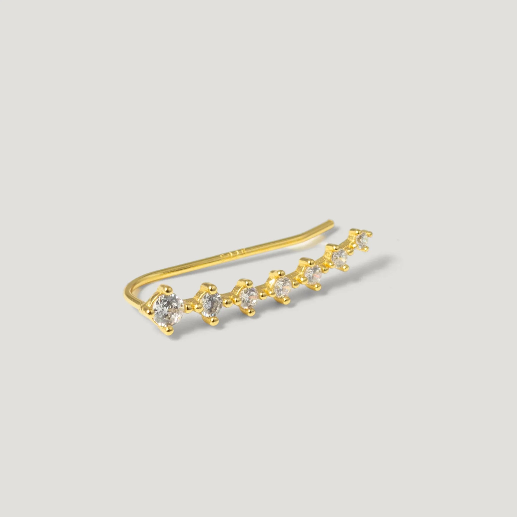 gold ear climber earring with seven round clear gemstones on light background