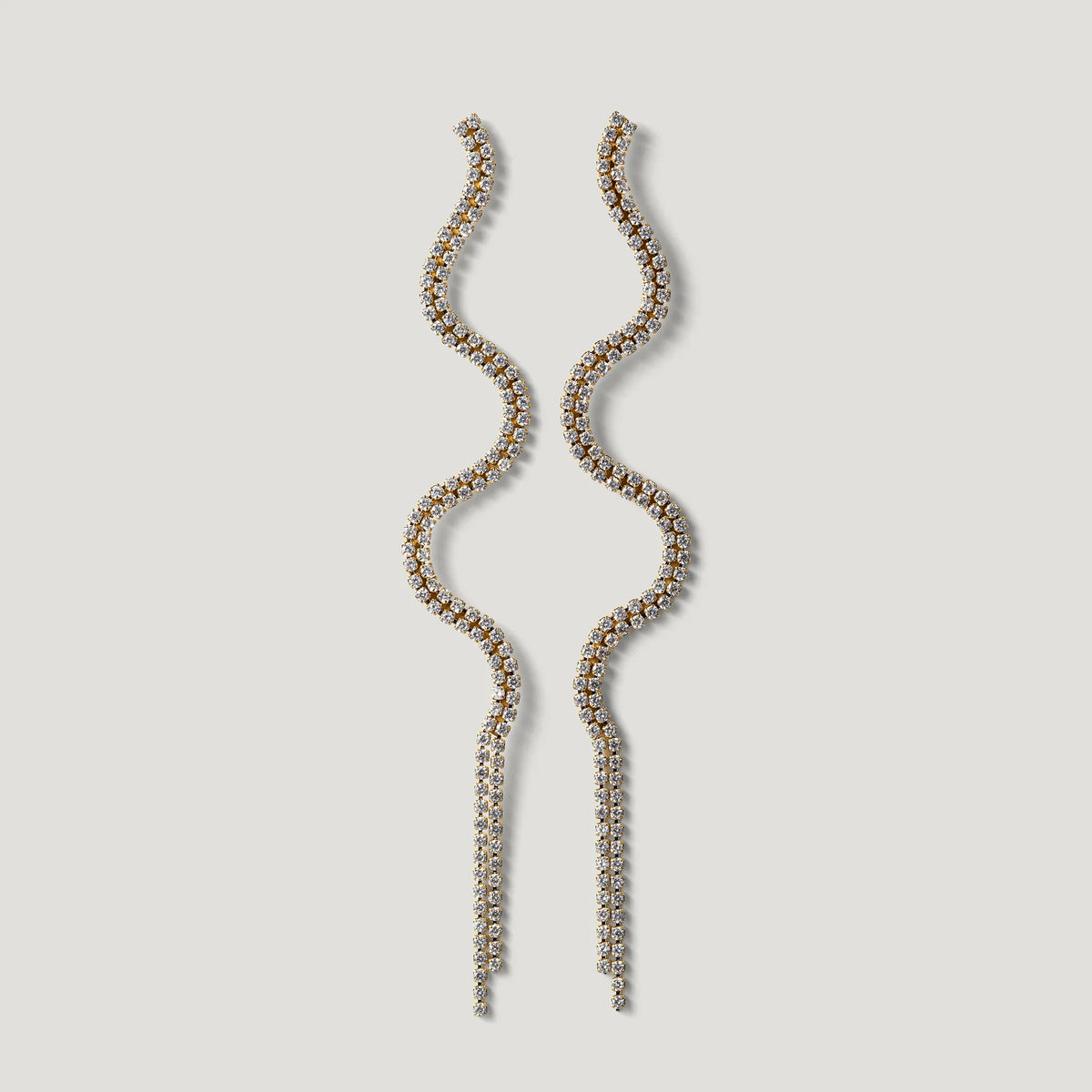 Long wavy gold earrings with clear crystals on a light background
