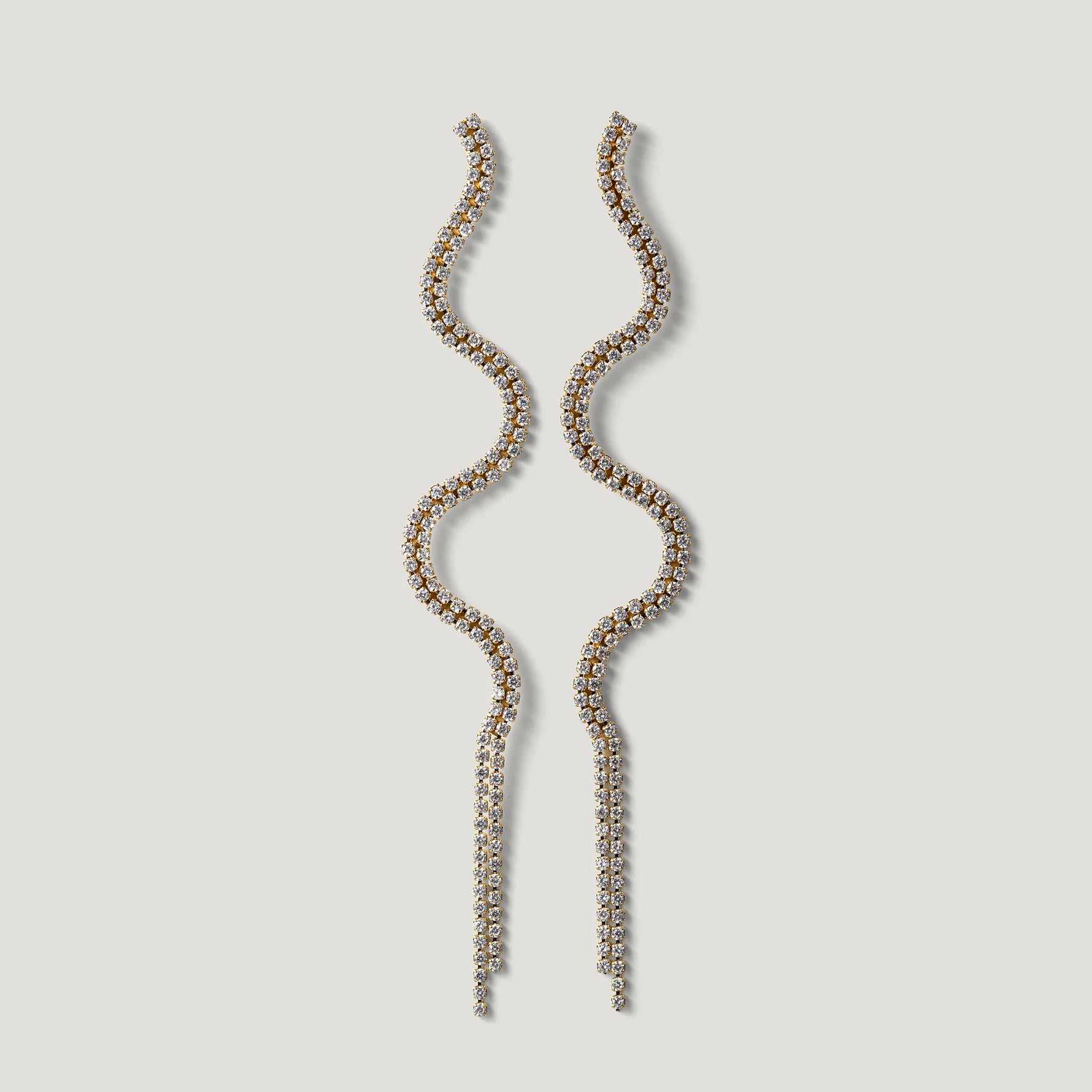 Long wavy gold earrings with clear crystals on a light background