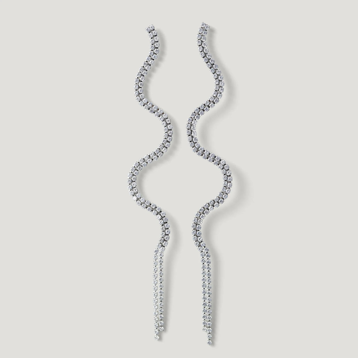 Wavy silver dangle earrings with sparkling crystals on a light background
