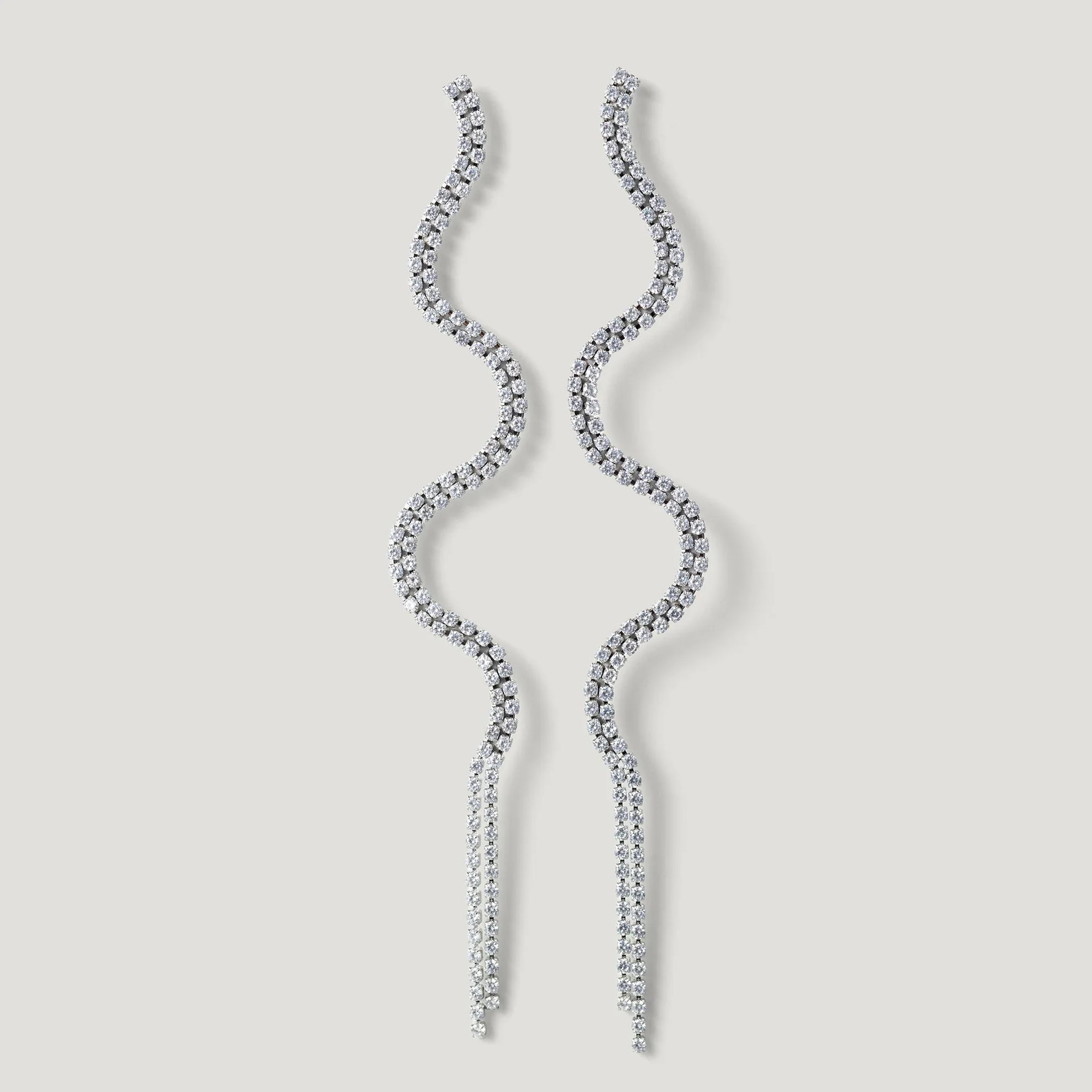Wavy silver dangle earrings with sparkling crystals on a light background