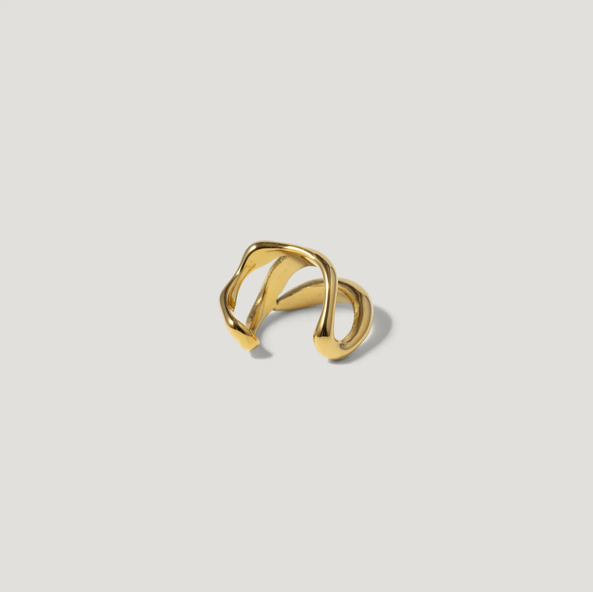 Gold open band ring with abstract, wavy design on a light background