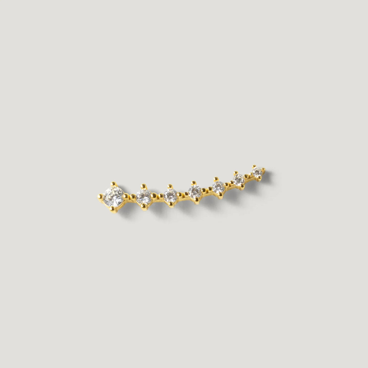 Gold ear climber earring with multiple round clear stones on a light background