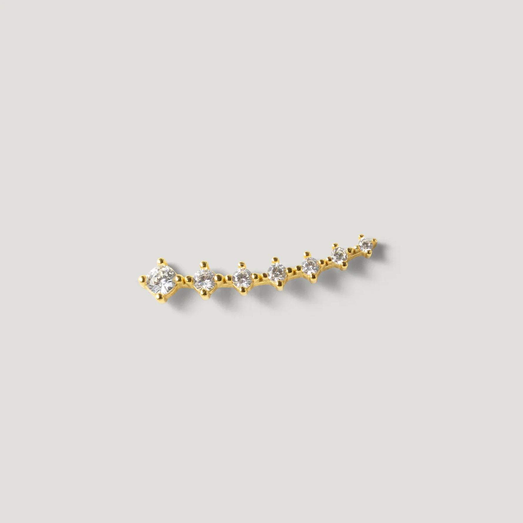 Gold ear climber earring with multiple round clear stones on a light background