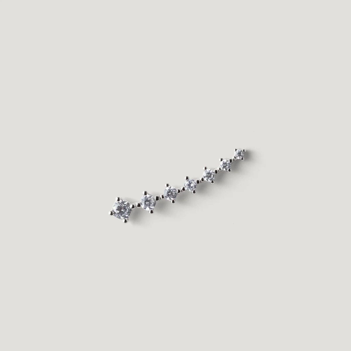 silver ear climber earring with seven small round white gemstones on neutral background