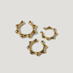 Three sculptural gold rings with organic, wavy shapes on a plain white background