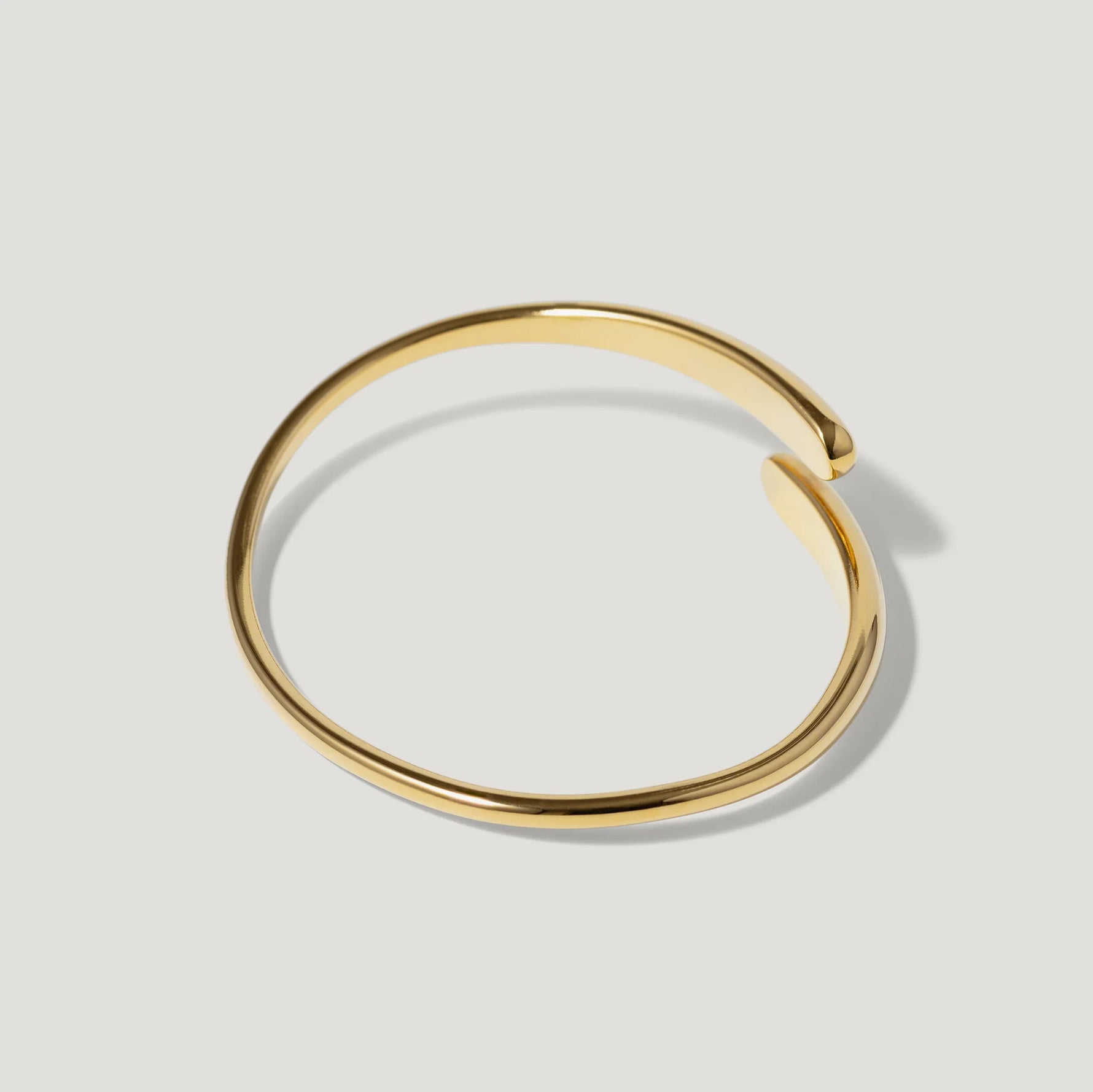 Minimalist open gold bangle bracelet on light background