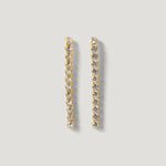 Gold drop earrings with vertical row of clear round gemstones on light grey background