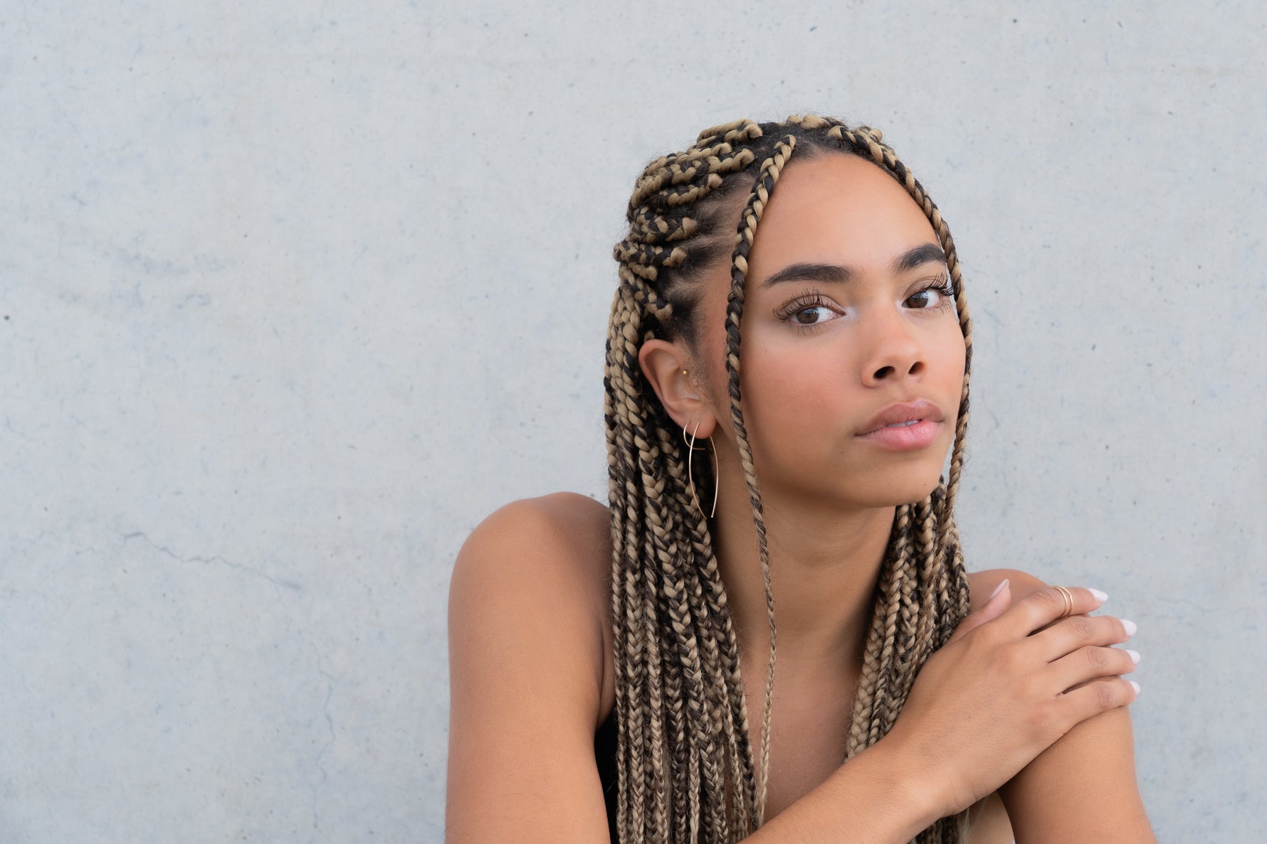 Woman with braided hair wearing a gold thread earring, hand resting on shoulder.