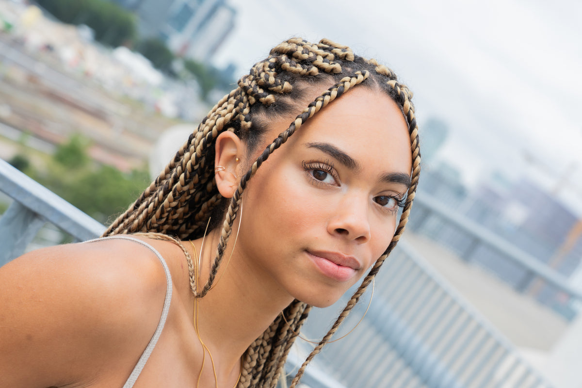 Close-up of a woman's neck and braided hair, wearing a fine gold chain necklace.