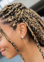 Close-up of woman's ear wearing a pearl stud earring with gold chain tassel, braided hair