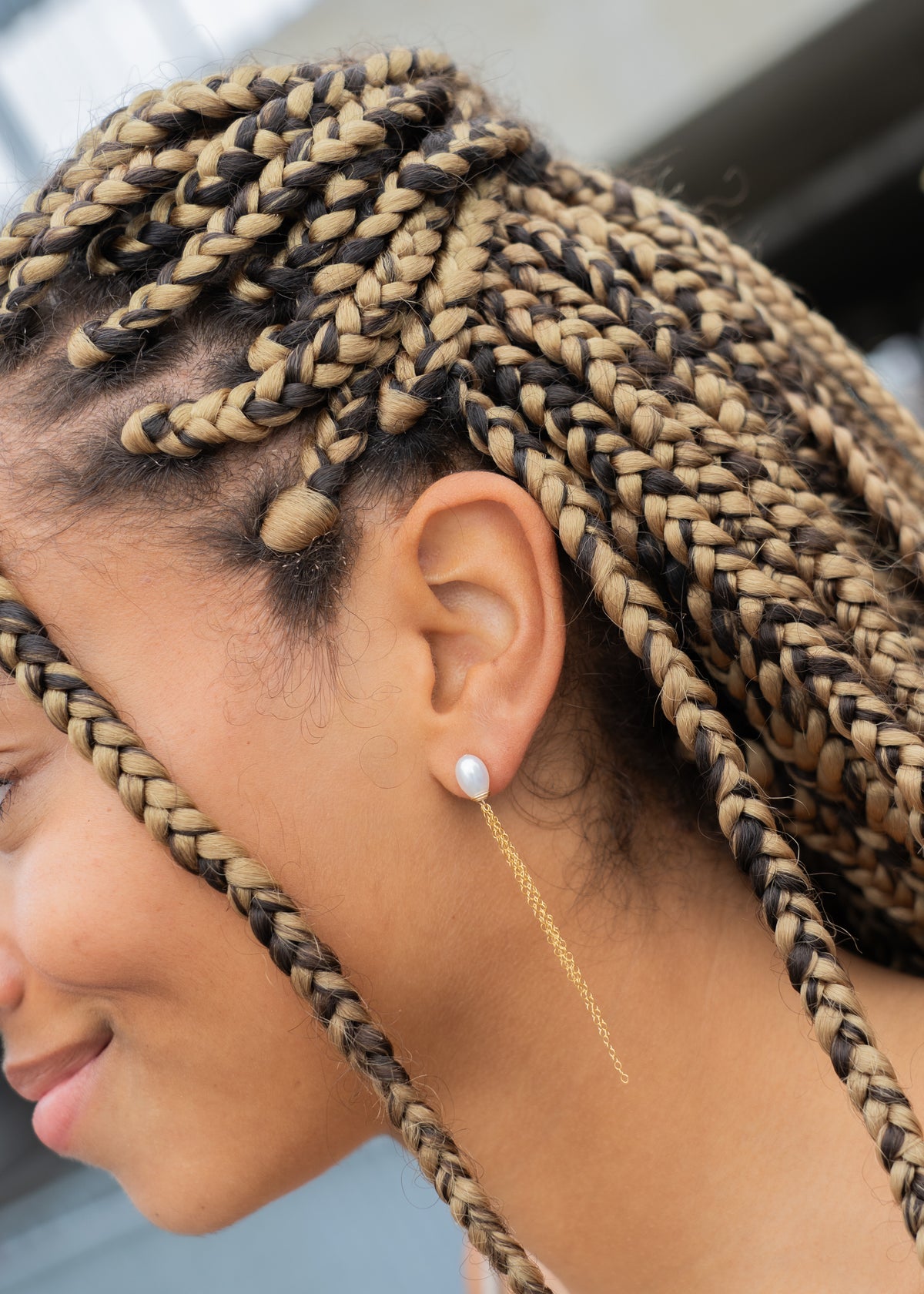 Close-up of woman's ear wearing a pearl stud earring with gold chain tassel, braided hair