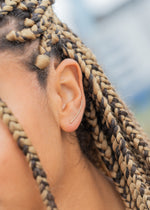 Extreme close-up of a woman's ear with braided hair, showing a thin gold ear climber.