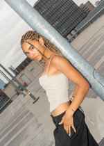 Woman with braided hair leaning on a pole, pearls visible dangling near her ear.