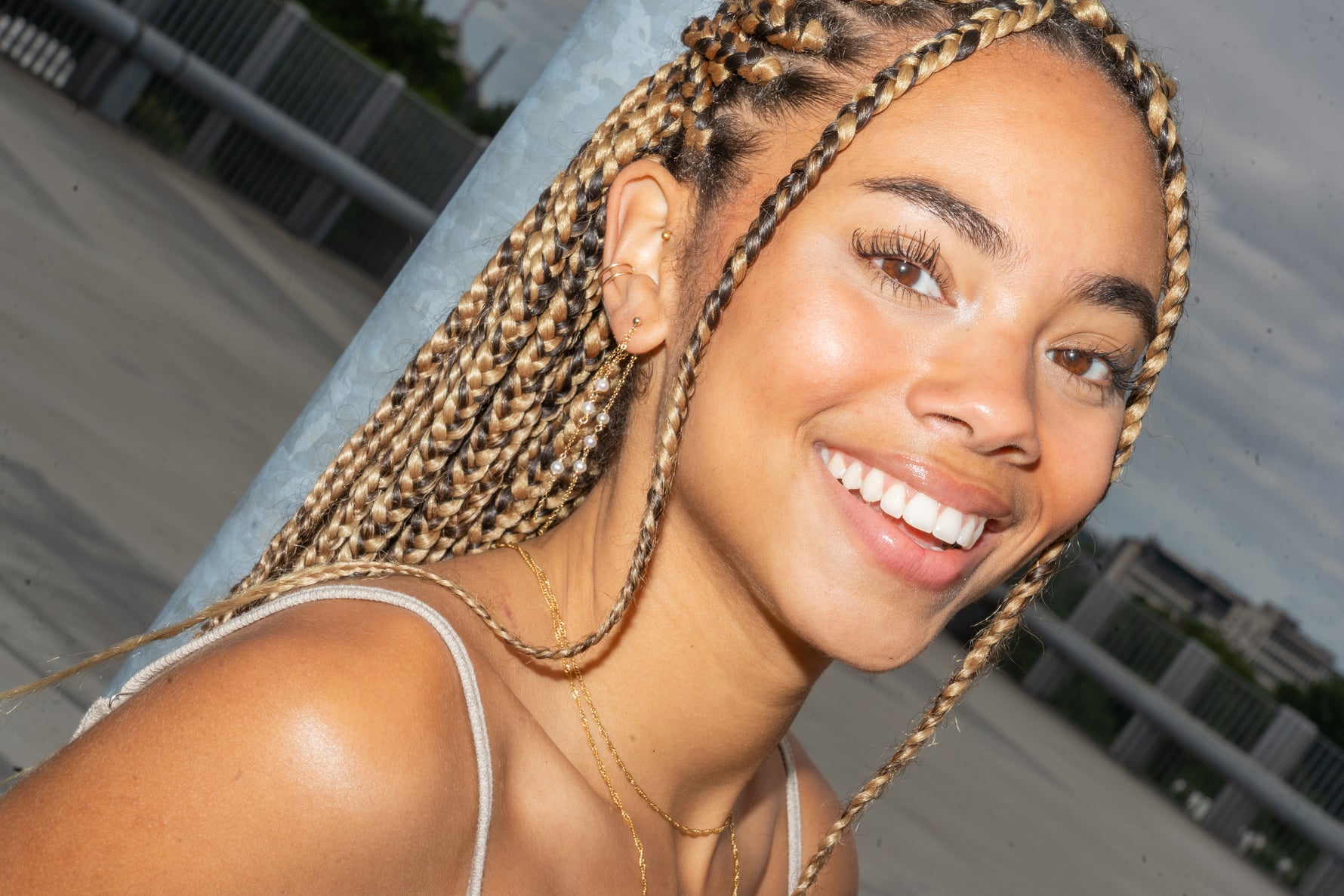 Close-up of smiling woman with multiple ear piercings, wearing a gold pearl drop earring.