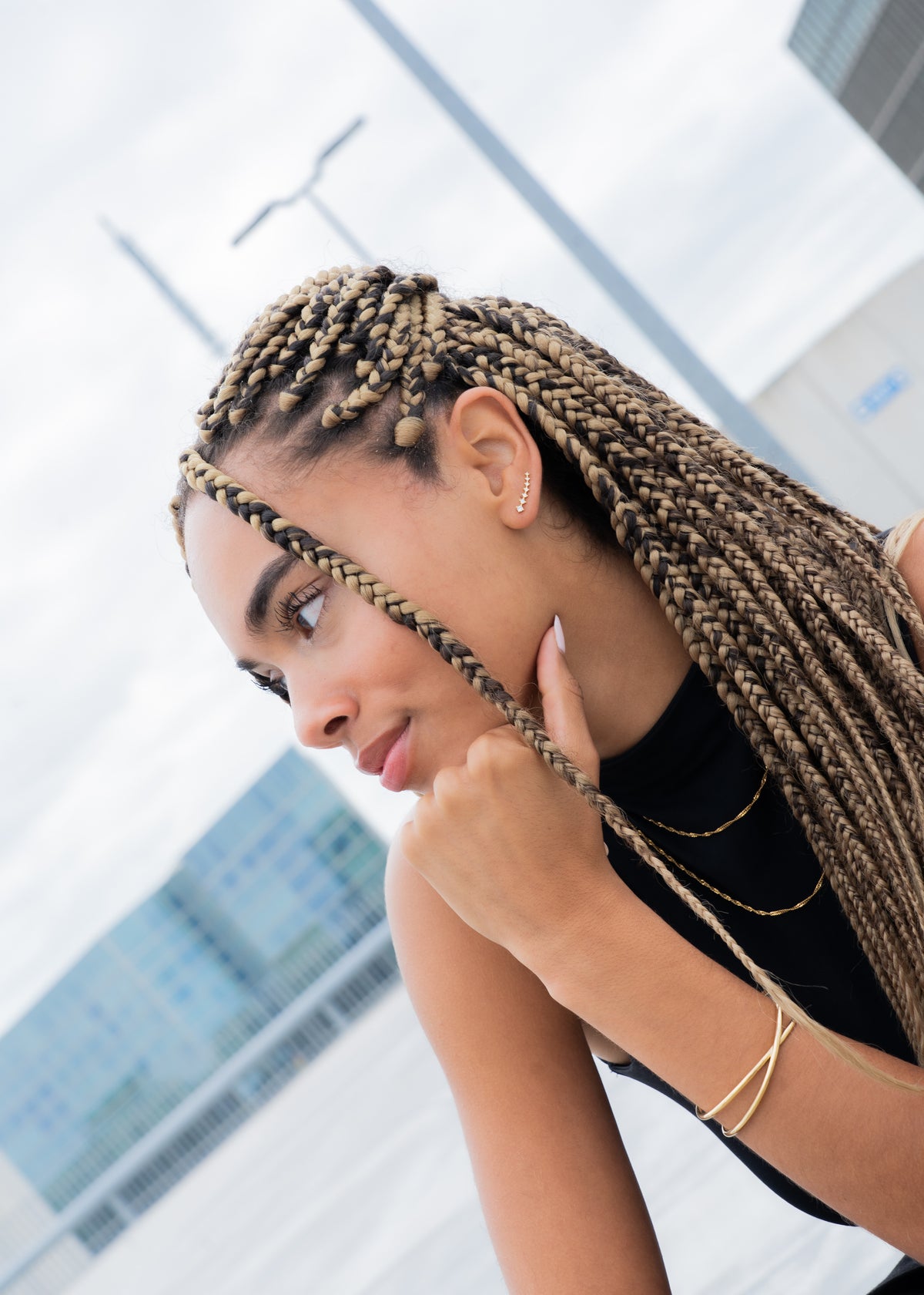 Woman wearing a gold ear climber, layered gold necklaces and a gold bangle, braided hair.