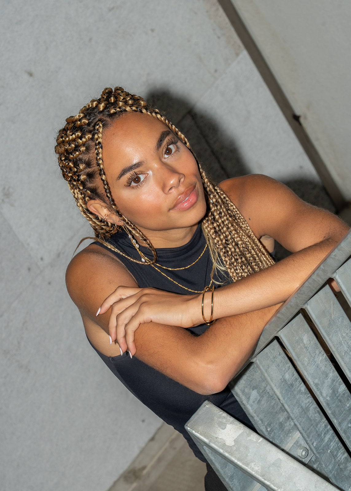 Woman with braided hair looking up, wearing a gold pearl drop earring, arms crossed.