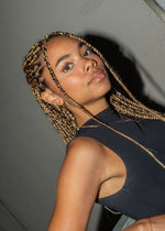 Woman with braided hair looking over her shoulder, wearing a gold pearl drop earring.
