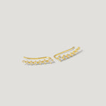Gold ear climber earrings with clear gemstones on a neutral background