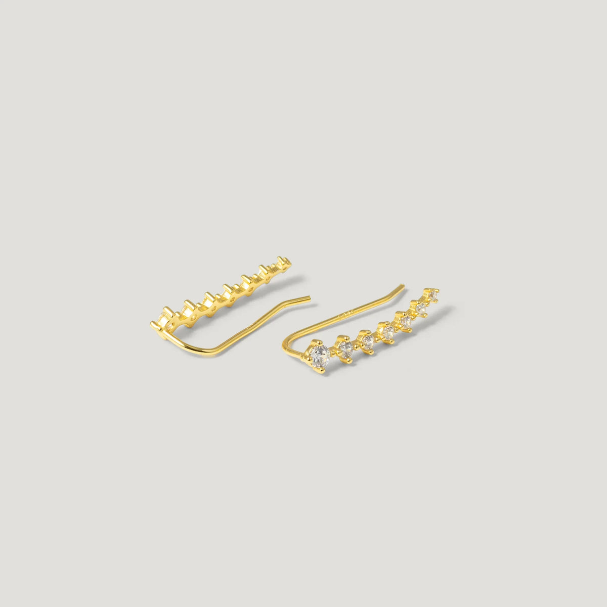 Gold ear climber earrings with sparkling white gemstones on a neutral background