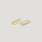 Gold ear climber earrings with sparkling white gemstones on a neutral background